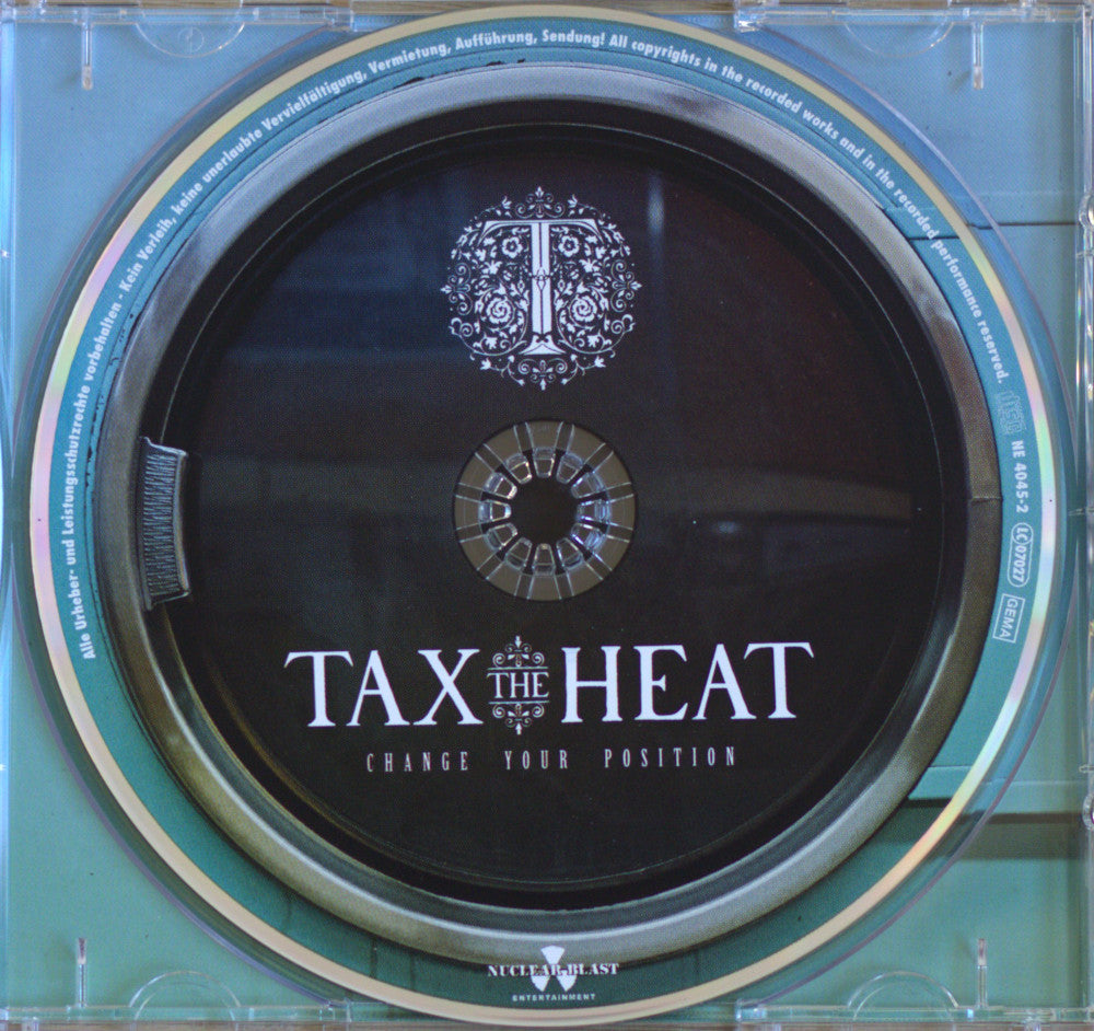 A CD jewel case containing a black disc with the title 'TAX THE HEAT' and the subtitle 'CHANGE YOUR POSITION' in white text, plus a decorative emblem above the title. The case rim is teal with gold-colored reflective bands.