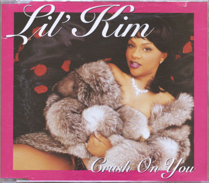 CD cover for Lil' Kim's single 'Crush On You', featuring a portrait of the artist wrapped in a gray fur coat against a dark background with red petals, framed by a pink border with white script text.