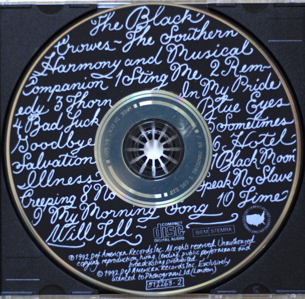 A close-up of a CD disc with handwritten-style blue text listing song titles around the outer ring, and the center label reading 'The Black Crowes' and 'BiM Stemma'.